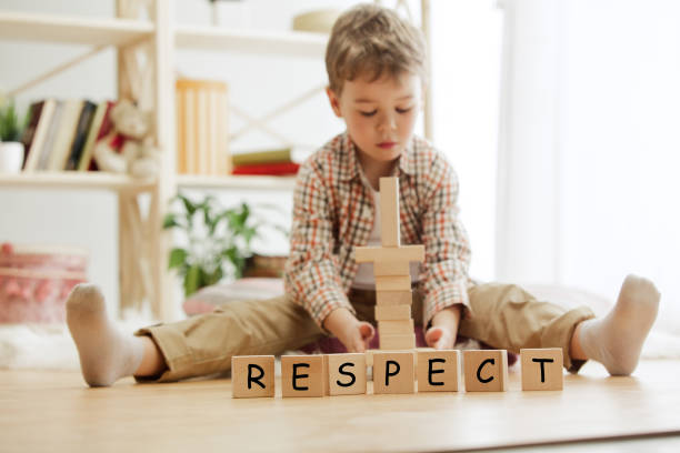Règles éducatives : un garçon assis les jambes écartées empile des cubes en bois derrière le respect