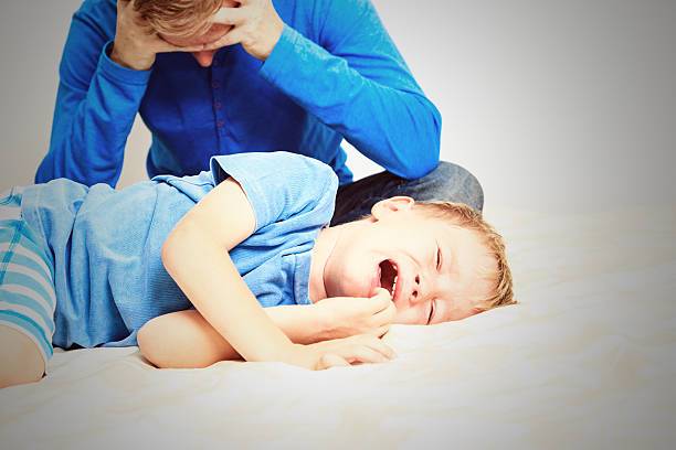 Enfant habillé en bleu, qui pleure allongé sur le côté. Le parent habillé en bleu se tient la tête dans les mains